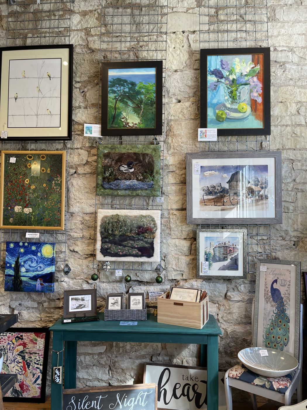 Framed paintings and felted wool art hung on the limestone wall inside Galeria Saro